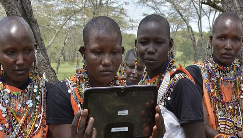 Group of people in traditional attire gathered around a tablet device
